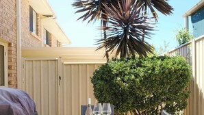 An outdoor patio with a table and chairs, a barbecue grill, and a large plant. - Sandy Shore Villa at Mollymook (Mollymook)