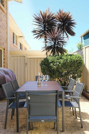 An outdoor patio with a table and chairs, a barbecue grill, and a large plant.