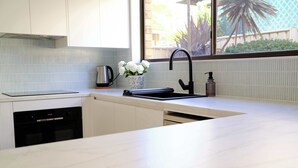 A modern kitchen with a built-in dishwasher, a black faucet, and a window with a view of greenery. - Sandy Shore Villa at Mollymook (Mollymook)