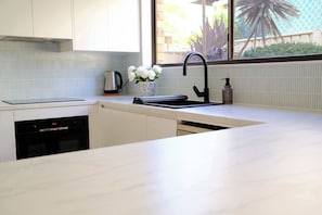 A modern kitchen with a built-in dishwasher, a black faucet, and a window with a view of greenery.
