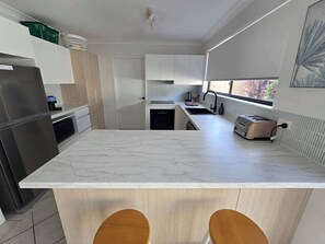 Une cuisine moderne dotée d’un plan de travail en marbre, d’appareils électroménagers intégrés et d’une fenêtre laissant entrer la lumière naturelle.