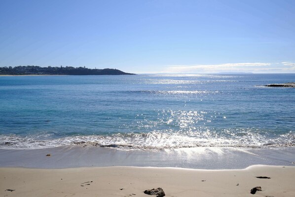 A beach with clear water, a sandy shore, and a distant landmass.