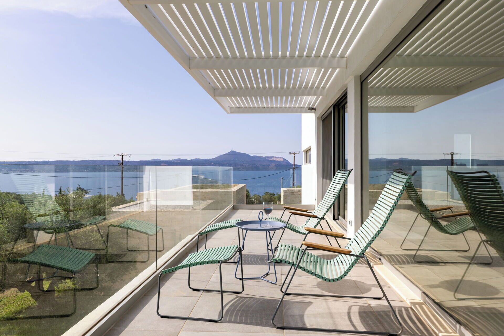 Ein Balkon mit Gartenmöbeln, einem Glastisch und Blick auf das Meer und die Berge.