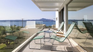 Ein Balkon mit Gartenmöbeln, einem Glastisch und Blick auf das Meer und die Berge.