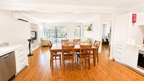 A spacious room with a wooden dining table and chairs, a white sofa, and a kitchen area with white cabinets. - Harbour Haven at Ulladulla (Ulladulla)