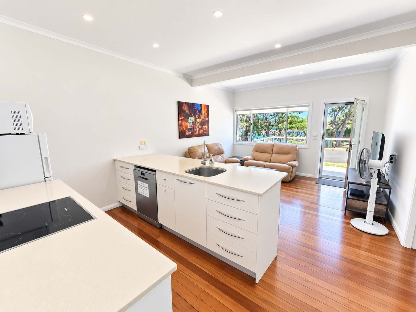 A modern kitchen with a dishwasher, a dining area with a sofa, and a view through a glass door.