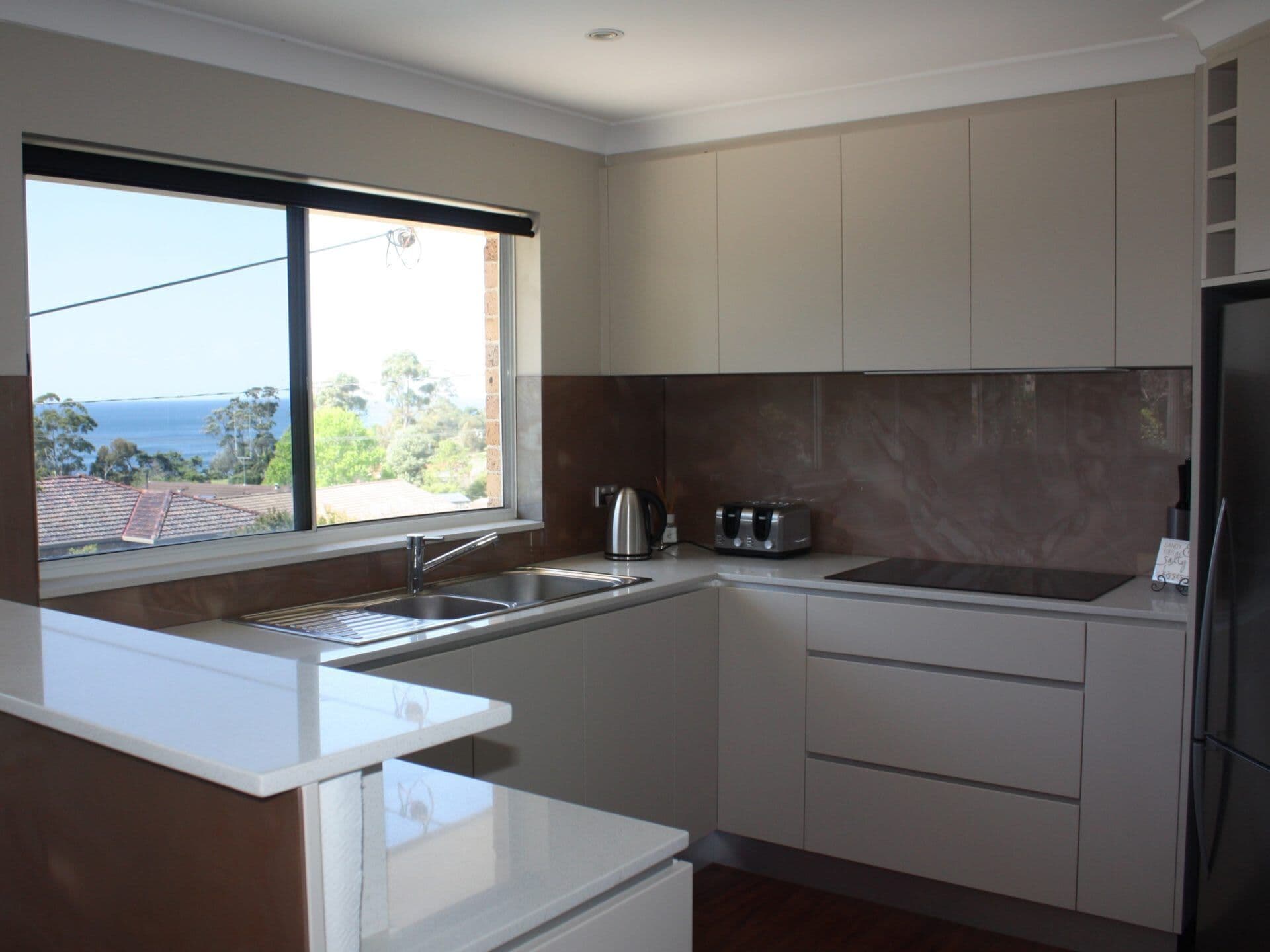 A modern kitchen with a large window, stainless steel appliances, and a view of the ocean.