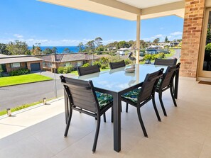 A glass-top table with six chairs, a brick wall, and a view of a residential area with houses and a clear sky.