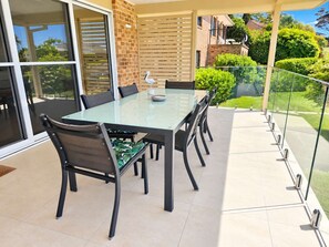 A glass-top dining table with chairs, a brick wall, and a view of a garden.