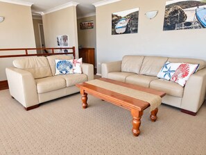 A living room with two beige sofas, a wooden coffee table, and nautical-themed wall art.