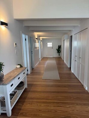 A long, narrow hallway with wooden flooring, white walls, and a central rug.