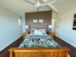 A bedroom with a bed, two bedside tables, a ceiling fan, and artwork on the wall.