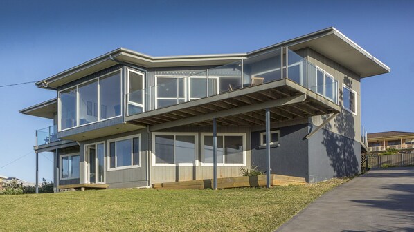 A modern two-story house with large windows, a balcony, and a covered outdoor area.