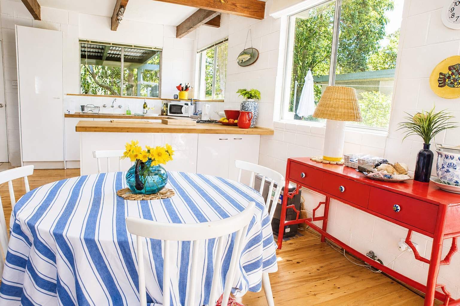 Een keuken met een eethoek, met een geruit tafelkleed, een vaas met bloemen en een rode kast.