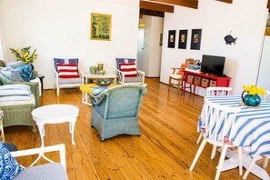 A living room with wicker furniture, a television, and artwork on the walls. - Kywong Beach Cottage (Bawley Point)