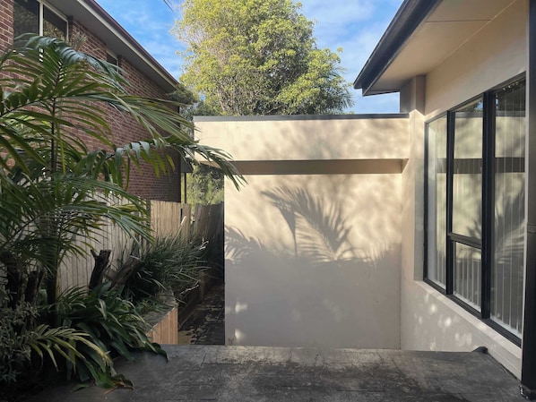 A modern building with a large window, a concrete pathway, and lush greenery.