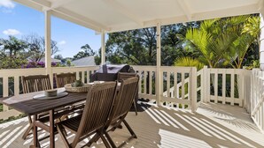 A covered outdoor patio with a wooden table and chairs, a grill, and a white fence. - Jillbys House at Narrawallee (Narrawallee)
