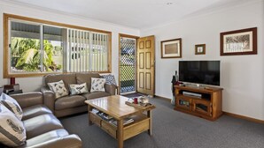 A living room with a sofa, coffee table, TV, and framed pictures on the wall. - Jillbys House at Narrawallee (Narrawallee)