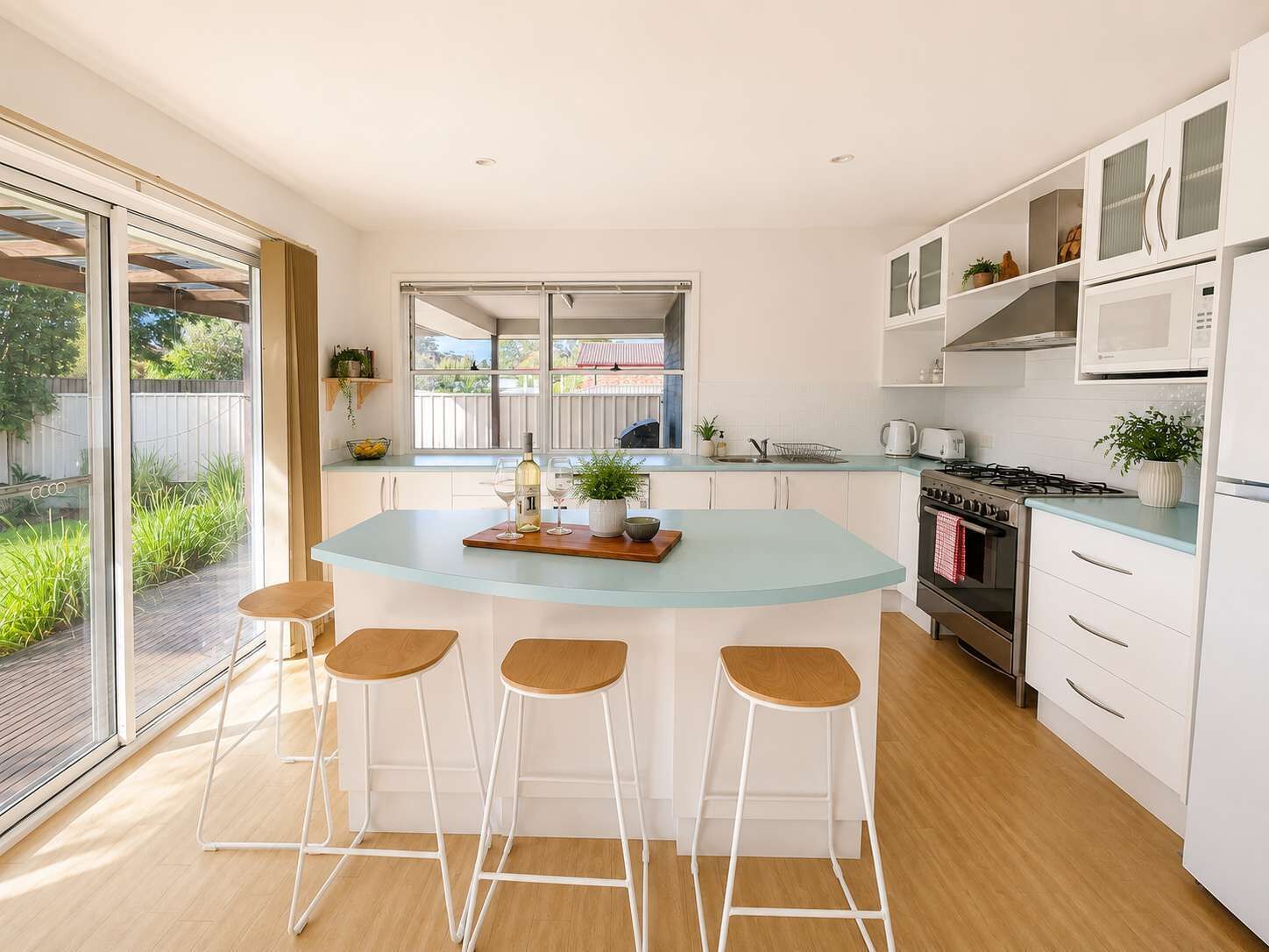 A modern kitchen with a central island, bar stools, a stove, and a large window.