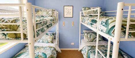A bunk bed room with a tropical leaf pattern bedspread, a framed inspirational quote on the wall, and a window with blinds.
