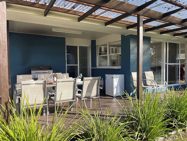 An outdoor patio with a grill, seating, and a refrigerator.