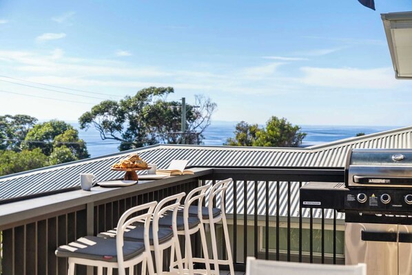 Une terrasse avec un barbecue, des chaises et une table où sont disposés de la nourriture et un livre.