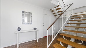 Een trap met houten treden en witte leuningen, een witte console tafel met decoratieve objecten, en een spiegel met een patroon aan de muur.