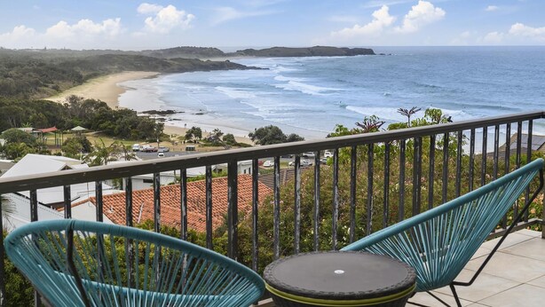 Een balkon met twee stoelen en een tafel, met uitzicht op een strand en de oceaan.