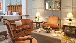 Une chambre d’hôtel comprenant un lit, deux fauteuils, une table basse, un miroir et deux lampes.