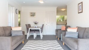 Ein Wohnzimmer mit zwei Sofas, einem Esstisch mit Stühlen, einem Teppich und einer durchgehenden Tür sichtbaren Küche.