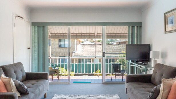 Ein Wohnzimmer mit zwei Sesseln, einem Fernseher und einer Glastür, die auf einen Balkon führt.