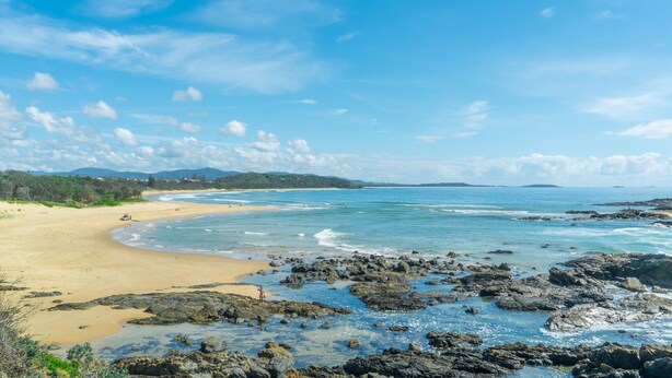 A beach with clear waters, rocky shoreline, and distant mountains. - Sand & Sea 5 - Beach at your Doorstep (Sawtell)