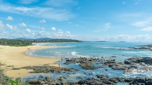 Une plage aux eaux cristallines, bordée d’une côte rocheuse et offrant une vue sur des montagnes lointaines.