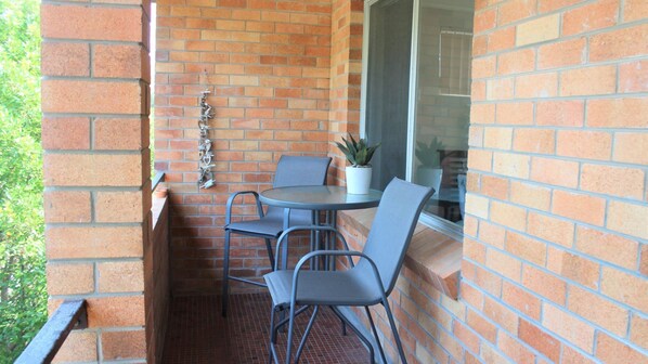 Un petit patio extérieur avec une table ronde et deux chaises, un pot de fleurs et un élément décoratif en métal fixé au mur de briques.