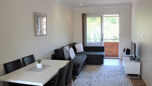 A modern living room with a dining table, a sofa, and a TV. - Sand & Sea 5 - Beach at your Doorstep (Sawtell)