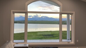 A large arched window with a view of a lake and mountains. - Brand new beautiful home with best view outside of Waterton Park. UPPER suite. (Mountain View)