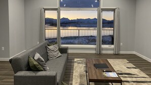A spacious living room with a large window overlooking a scenic landscape, a gray sofa, and a wooden coffee table. - Brand new beautiful home with best view outside of Waterton Park. UPPER suite. (Mountain View)