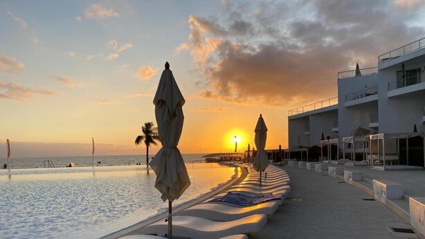 Un hôtel situé en bord de mer, doté de chaises longues et de parasols le long de la promenade, avec vue sur l’océan.