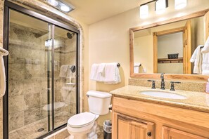 Un bagno con doccia vetro, un water, un lavandino con mobile impiallacciato e uno specchio sopra il lavandino.