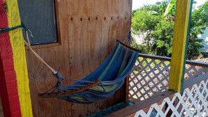 A wooden structure with a hammock hanging on a lattice railing, a window, and a view of greenery. -  Relax N SunShine 
Peaceful, Retreat (May Pen)