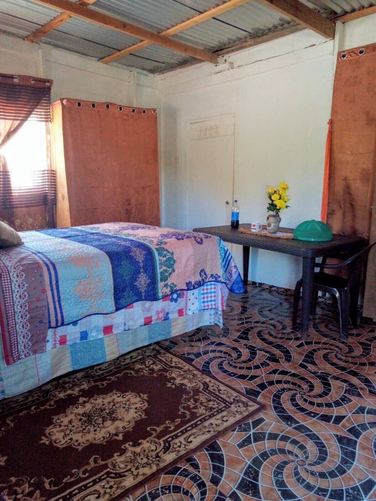 Een kamer met een bed, een tafeltje met een bloemenvaas en een stoel.