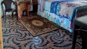 A bedroom with a bed, a chair, a small table with a vase, and a patterned rug. -  Relax N SunShine 
Peaceful, Retreat (May Pen)