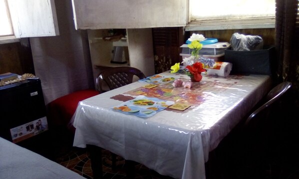 Comedor con una mesa cubierta por un mantel plástico, con un centro de mesa floral y un mantel individual con ilustraciones de comida.