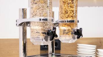 Eine Kaffeemaschine mit mehreren Ausgabespendern, eine Obstschale und gestapelte Teller auf einer Arbeitsfläche.