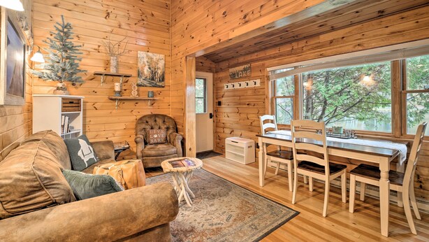 L’intérieur chaleureux d’un chalet avec un décor en bois, une table à manger avec des chaises, un canapé, une petite table d’appoint et un sapin de Noël.