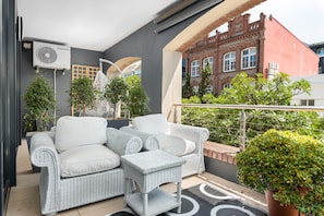 A balcony with wicker furniture, a potted plant, and a view of a red brick building. - Rockwell 114 (Cape Town)