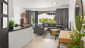 A modern living room with a grey sofa, a wooden coffee table, and a dining area. There is a large window with curtains, a plant, and a wall-mounted mirror. - Rockwell 114 (Cape Town)