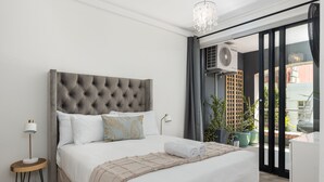 A modern bedroom with a tufted headboard, a neatly made bed, a bedside lamp, and a large window with a view of the city. - Rockwell 114 (Cape Town)