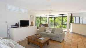 Relax in this stylish living room with a flat-screen TV, comfortable sofa, and a view of lush greenery outside.