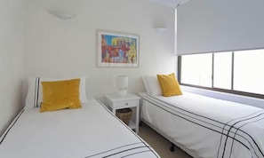 Una camera d'albergo con due letti, un comodino, una lampada e una finestra con persiane.